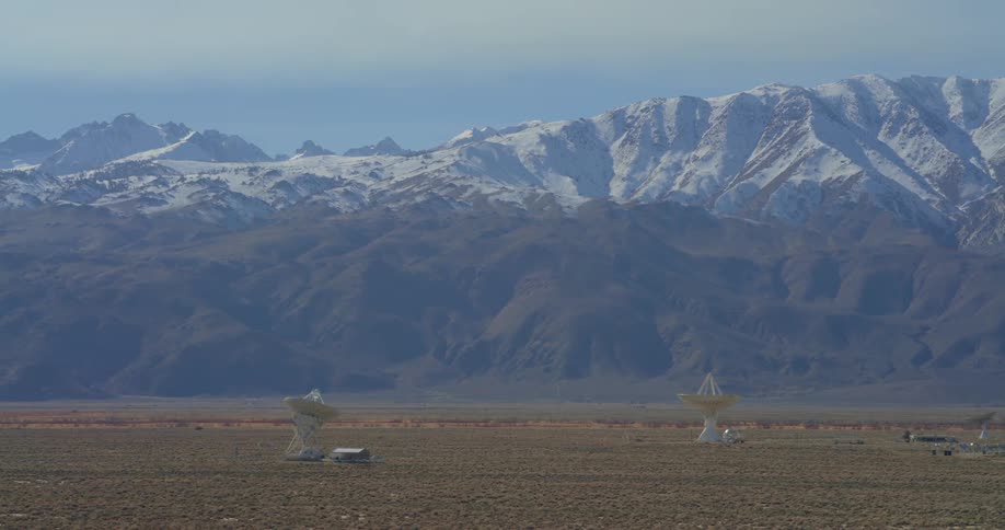 Satellite dishes on an arid plain with a snowcovered mountain range in the background