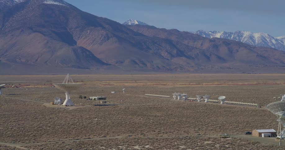 Satellite dishes in a desert plain with mountains in the background under a clear sky