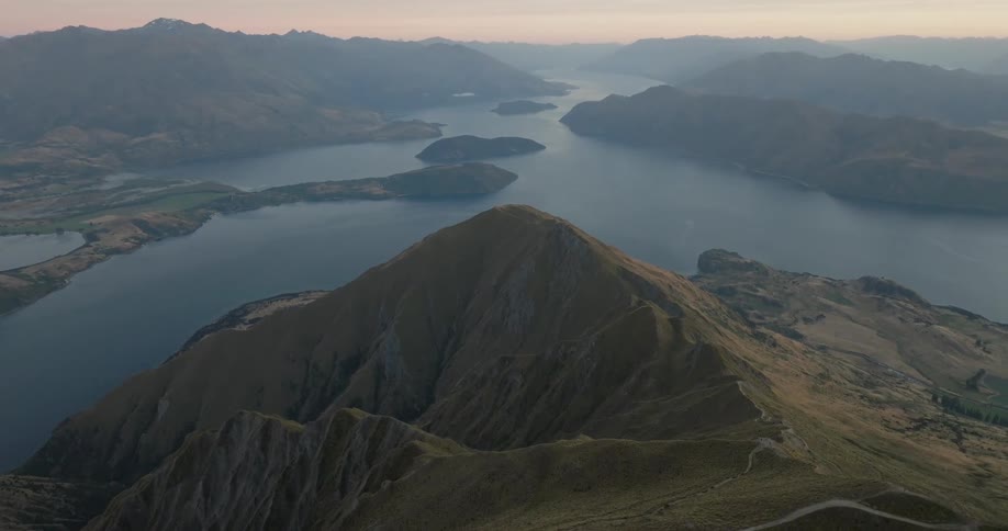 Aerial view of a mountain with a winding lake between mountain ranges in the background