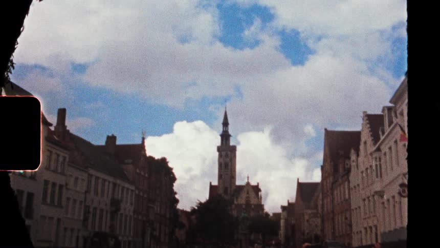 Historic street with aligned buildings and a central tower under a partly cloudy sky