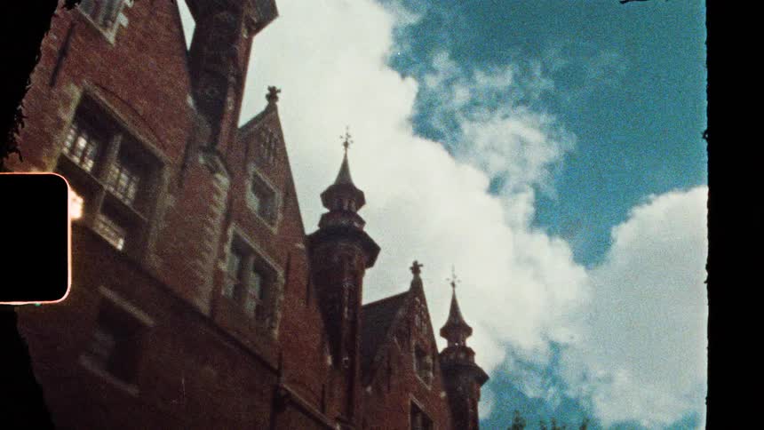 Brick facades with arched windows and towers under a partly cloudy sky