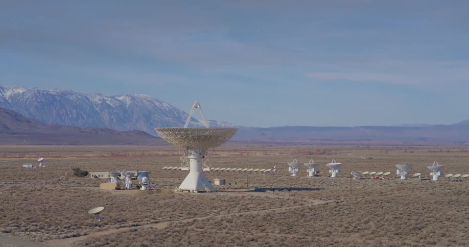 Large satellite dish surrounded by smaller ones on a desert plain with mountains in the background