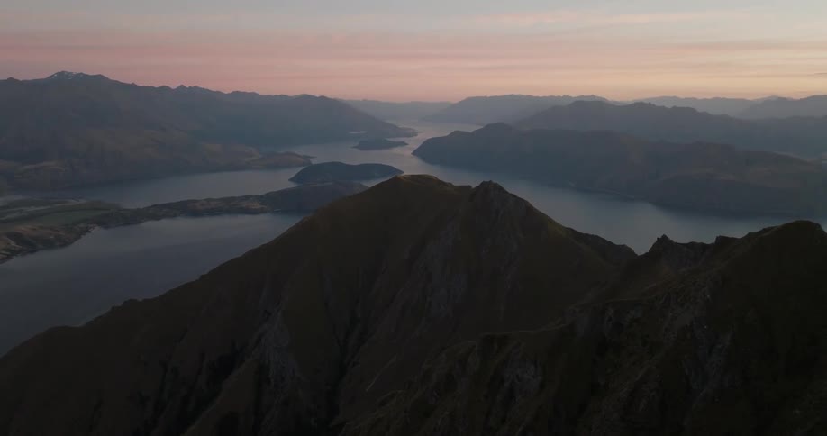 Mountain peaks in shadow with a lake in the background under evening light