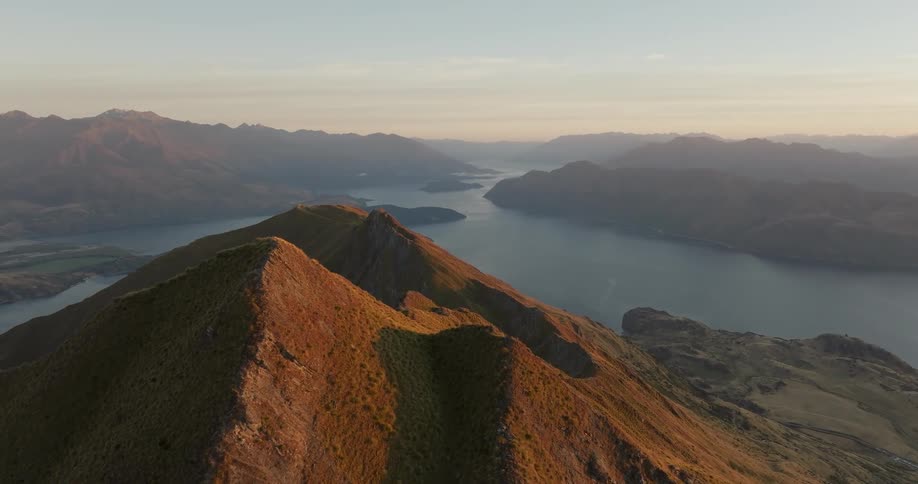 Sunlit mountain ridge with a winding lake and mountain ranges in the background