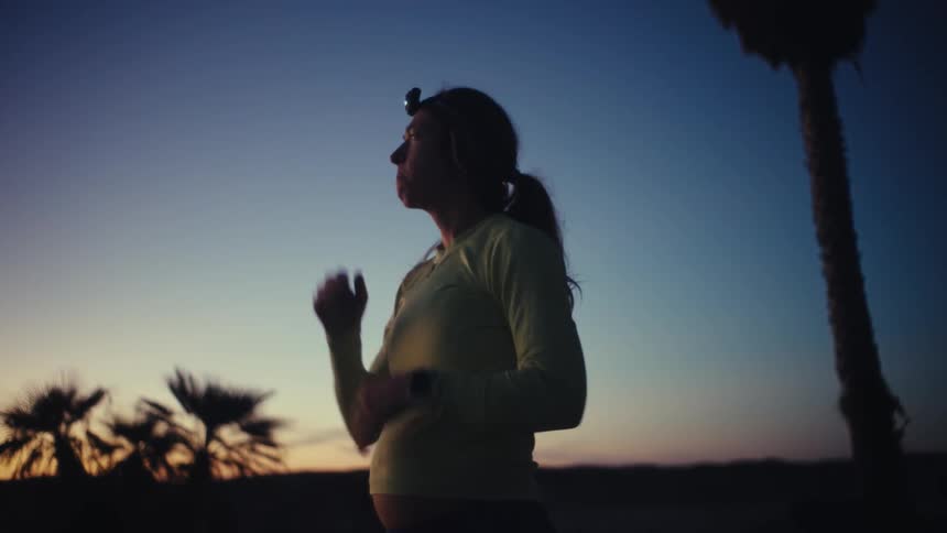 Pregnant woman wearing a headlamp rests her hands on her abdomen at dusk