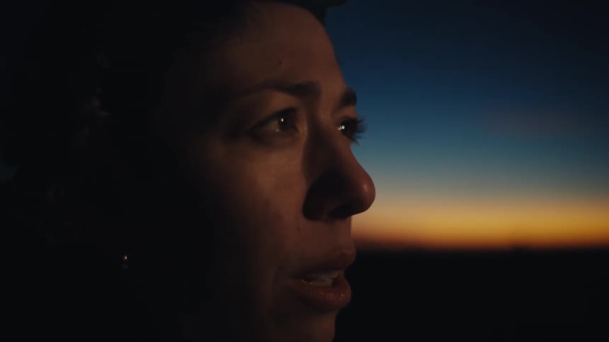 Pregnant woman wearing a headlamp holds her abdomen at dawn under an orangetoned sky