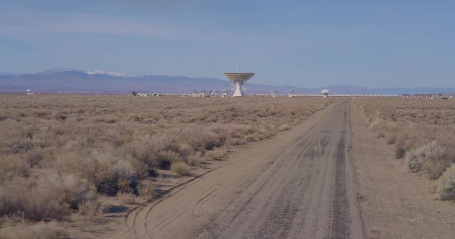 Dirt road near radio telescope antenna dishes in the desert with mountains in the distance