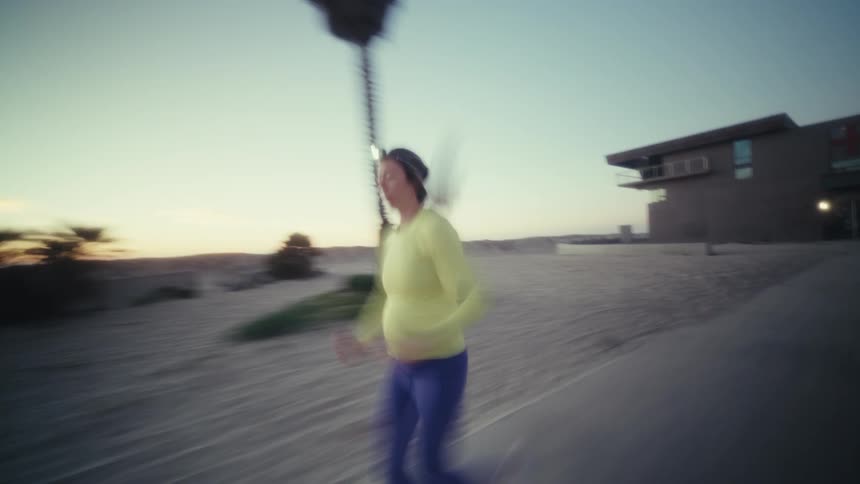 Pregnant woman runs at dusk wearing a headlamp in an open area with a palm tree in the background
