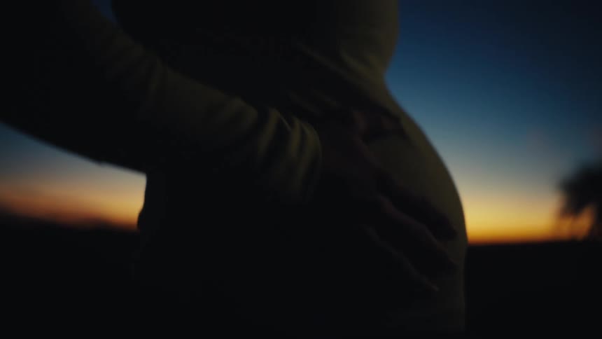 A pregnant woman wearing a yellow shirt and a lit headlamp stands outdoors at night