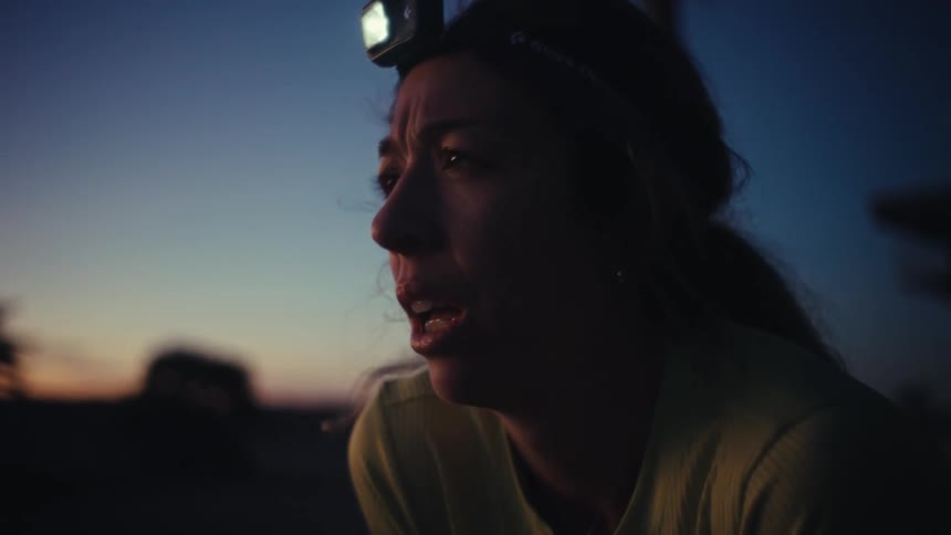 Person wearing a headlamp looks toward the horizon at dusk while taking a deep breath