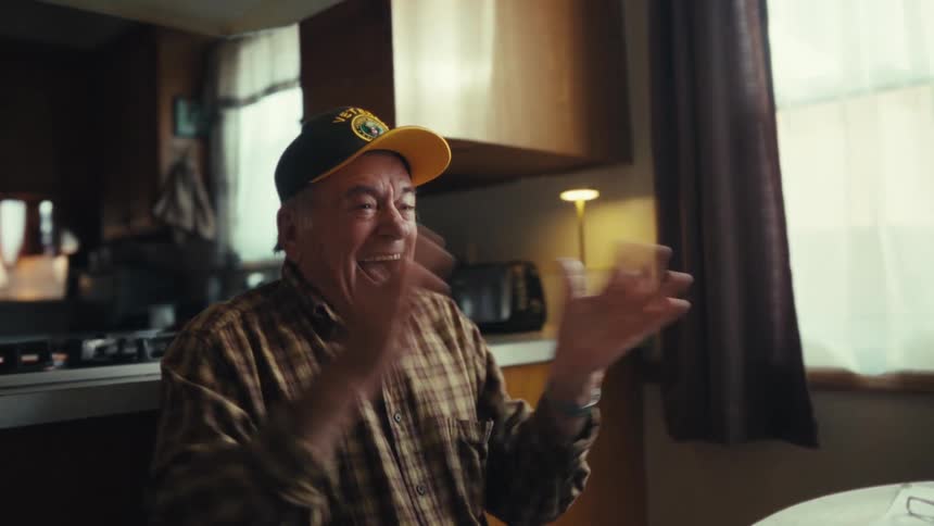 An elderly veteran cheers excitedly while looking at his laptop screen indoors