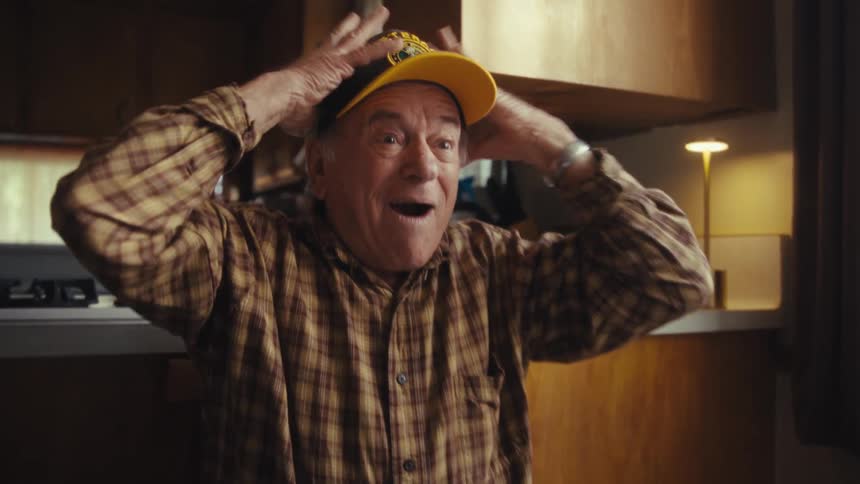Elderly man with veteran cap clapping in home kitchen