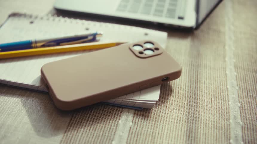 Man picks up a smart phone sitting on a notebook next to a laptop computer