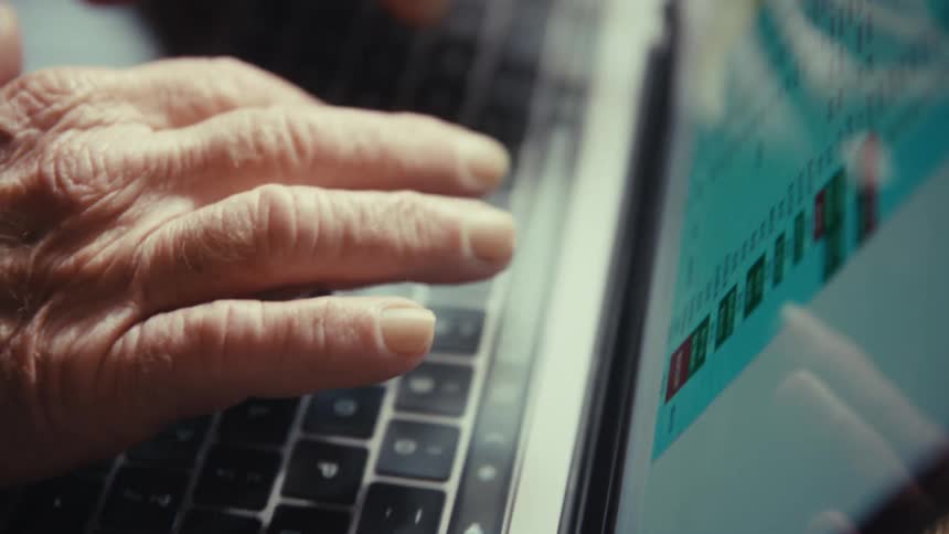 Man sitting at a table typing on the keyboard of a laptop computer