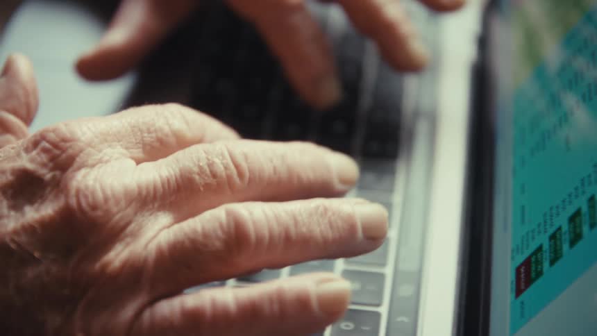 Hands type on a laptop with a spreadsheet displayed on the screen
