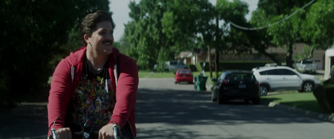 Smiling man riding a bicycle down a city street