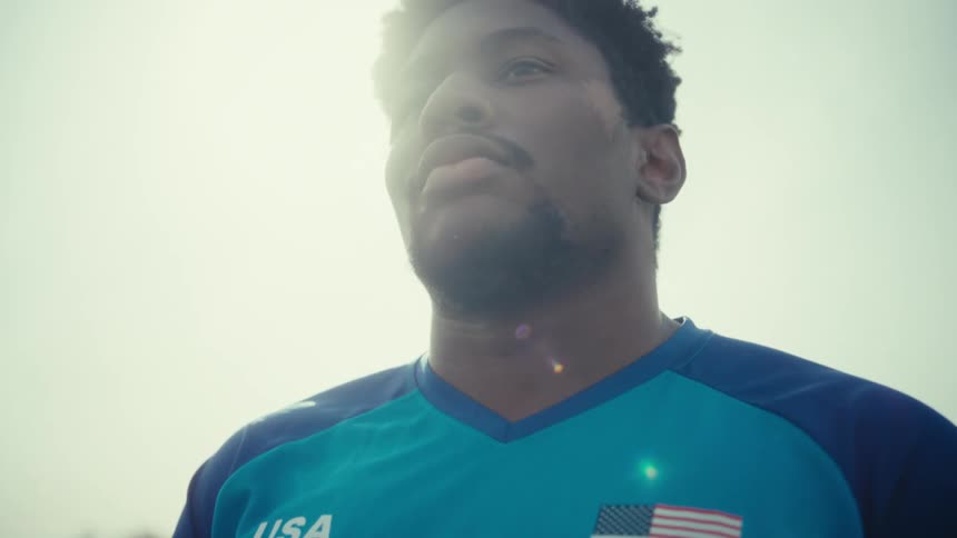 A man wearing a blue usa jersey looks up thoughtfully as the sun shines brightly behind himthe camera moves into a closeup of his face capturing a determined and focused expression against the bright sky