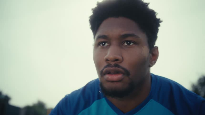 Soccer player looks across the field with a focused expression under sunlight