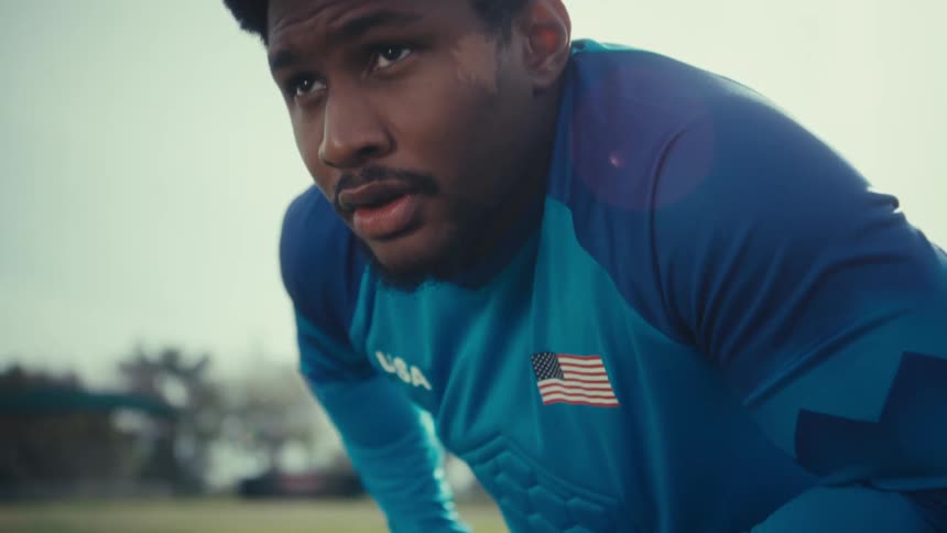 A soccer goalkeeper in a blue usa jersey holding a soccer ball while standing on a grass field he looks directly into the camera with a focused expression as he shifts the ball between his gloved hands
