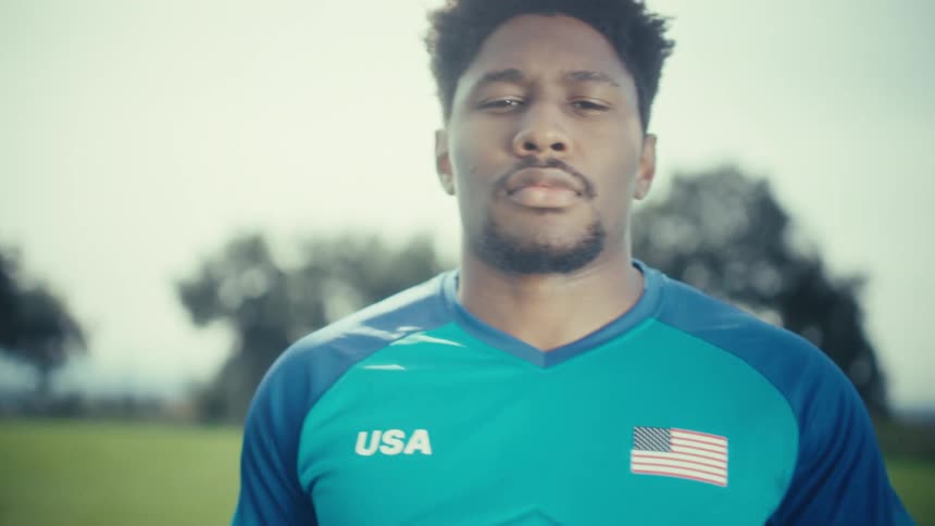 Soccer player stands in the field holding a soccer ball as he turns around to look at the camera