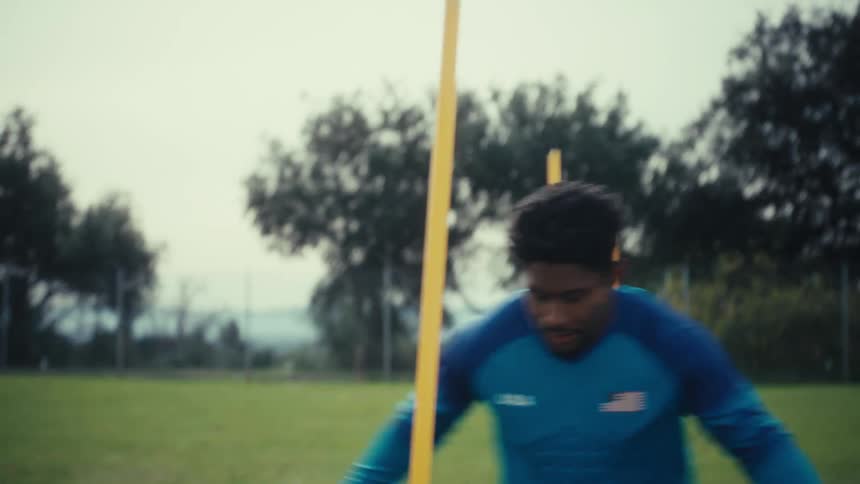 The man kicks the soccer ball around the poles