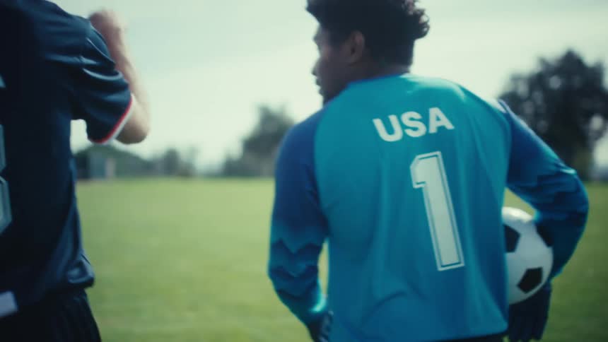 A view from behind shows two soccer players wearing jerseys with usa on the back as they walk together across a grassy field