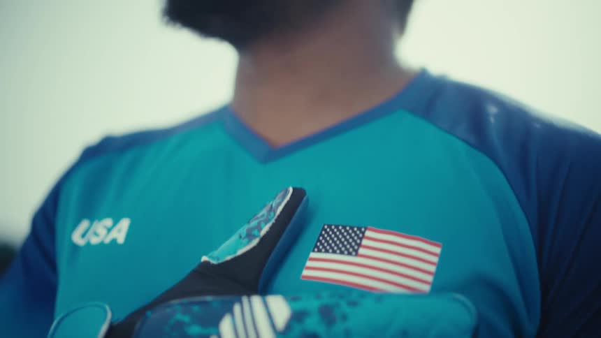 A soccer goalkeeper as he prepares for a moment of competition or reflectionthe camera begins with a closeup on his chest highlighting a usa flag patch and a gloved hand held over his heart before tilting up to capture his determined facial express
