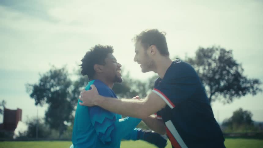 Two soccer players share a friendly greeting on a sunny field starting with a firm handshake that leads into a brief spirited hug the camera zooms in close on their clasped hands as they pull away highlighting their camaraderie