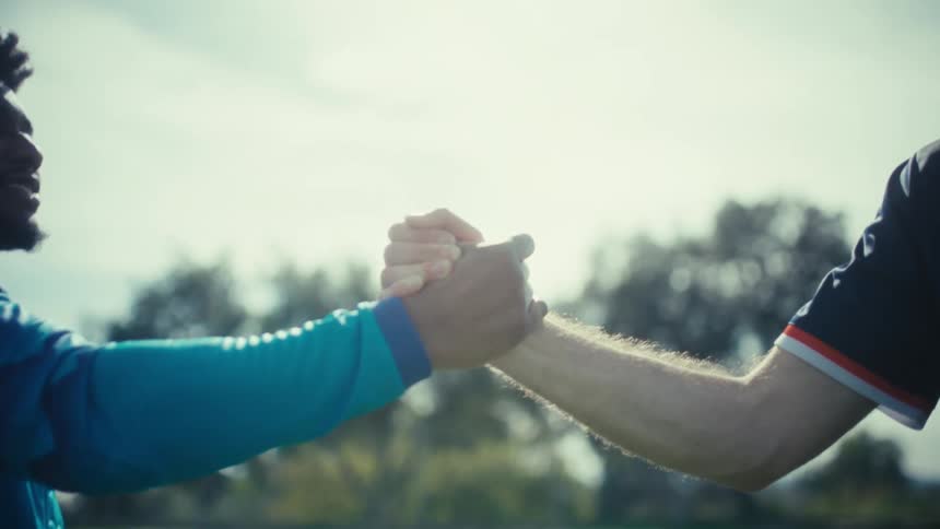Two young athletes on a field shaking hands and hugging at midday