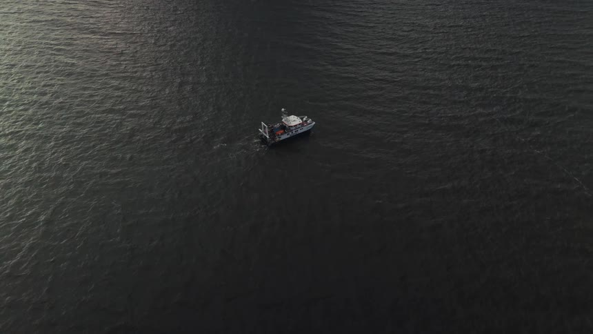 An aerial view shows a boat moving through the dark water of a large lake or ocean