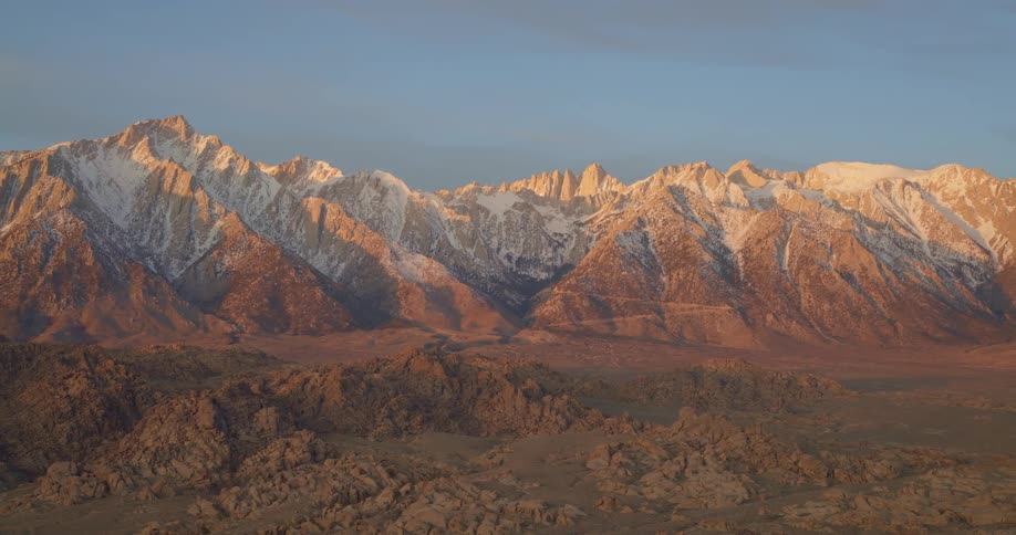 Snowcovered peaks lit by sunlight above arid rocky terrain