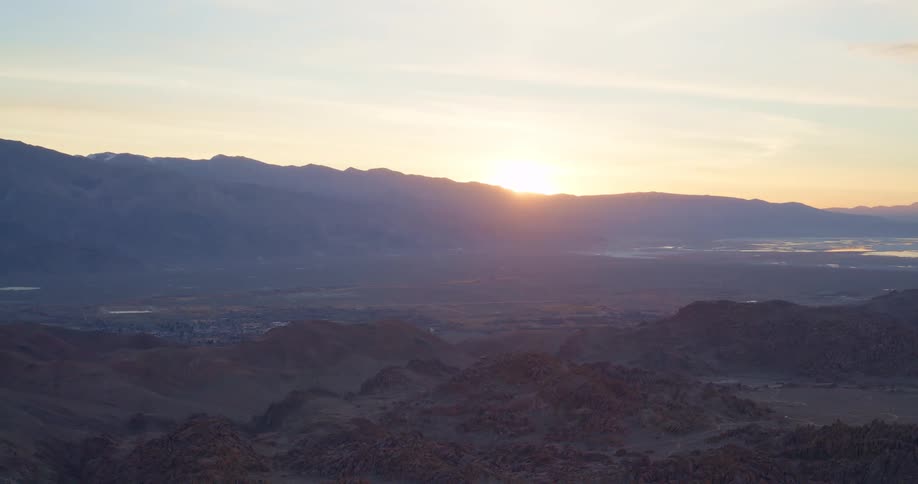 An aerial view shows the sun rising over a mountain range and a vast desert valley