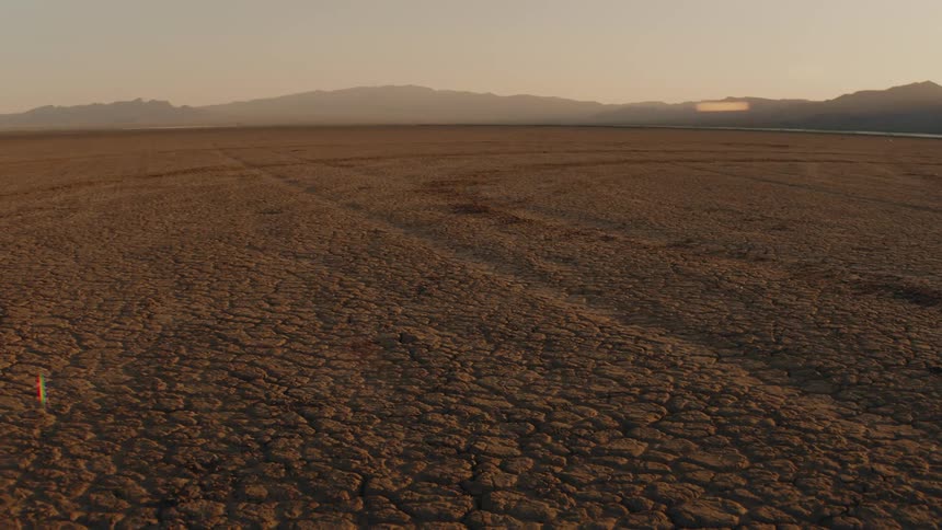 Arid plain with cracked ground and mountain range in the background under golden light