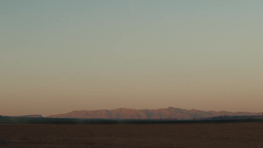 Flat barren field with mountains in the background under soft sunset light
