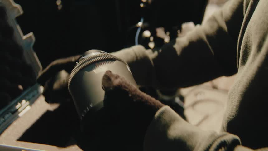 A person wearing gloves carefully removes a professional camera lens from a protective hardshell gear casethe individual prepares to attach the lens to a highend cinema camera rig mounted on the tailgate of a vehicle