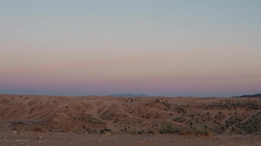 A vast expanse of rolling desert dunes stretches beneath a soft pastel sunset sky fading from pink to blue