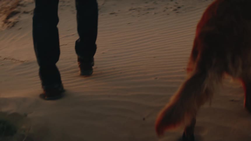 Person walking on sandy ground accompanied by golden retriever
