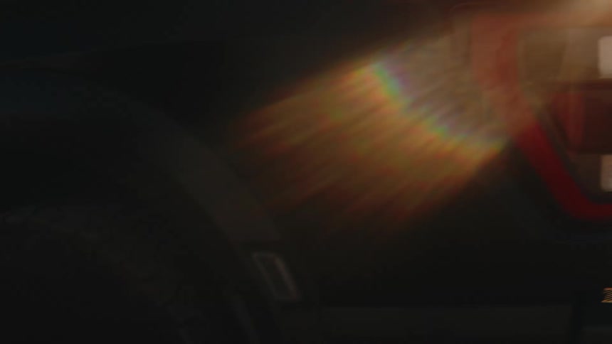 A man walks out of his truck then goes to the back to take boxes out of the trunk while parked in an open field at sunset