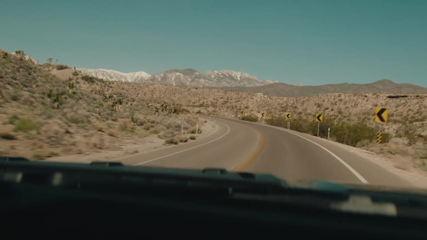 Curving desert road with direction signs in front of snowy mountains