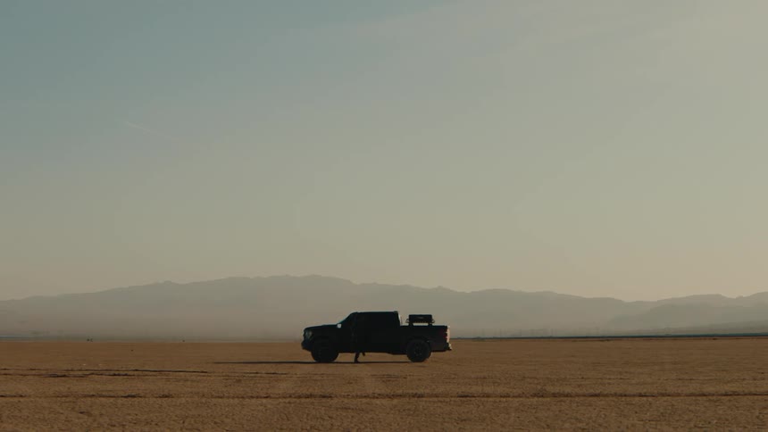 Truck stops in the desert and a man gets out with his dog and walks to the back of the truck