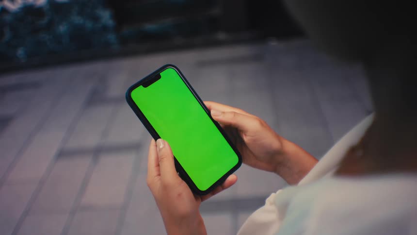 Person holding smartphone with green screen in urban setting