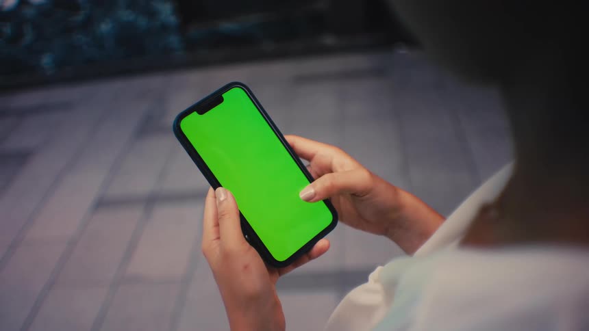 Person holding smartphone with green screen in urban setting
