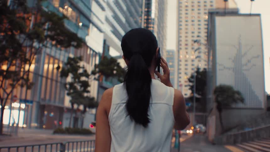 Woman with tied hair walking and talking on phone in modern urban area