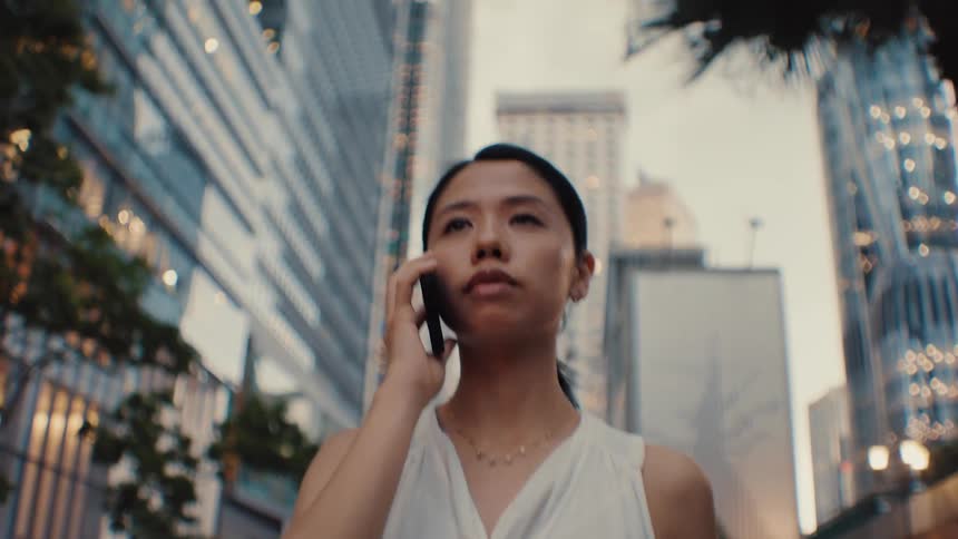 Woman in white top on phone among modern city buildings