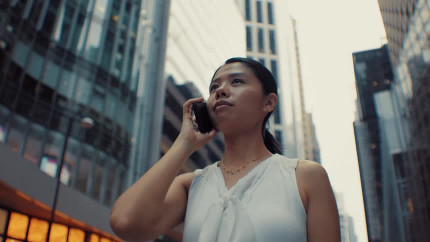Woman in white blouse on phone in urban street surrounded by modern buildings