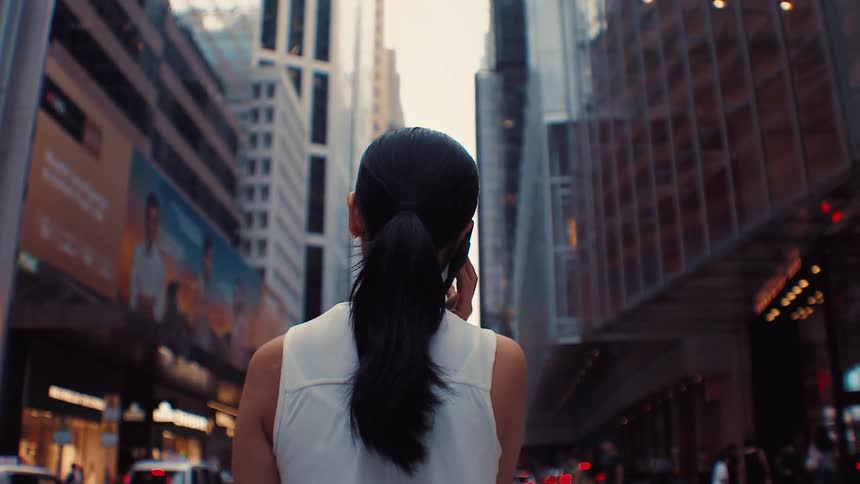 Woman with tied hair talking on phone in busy city street