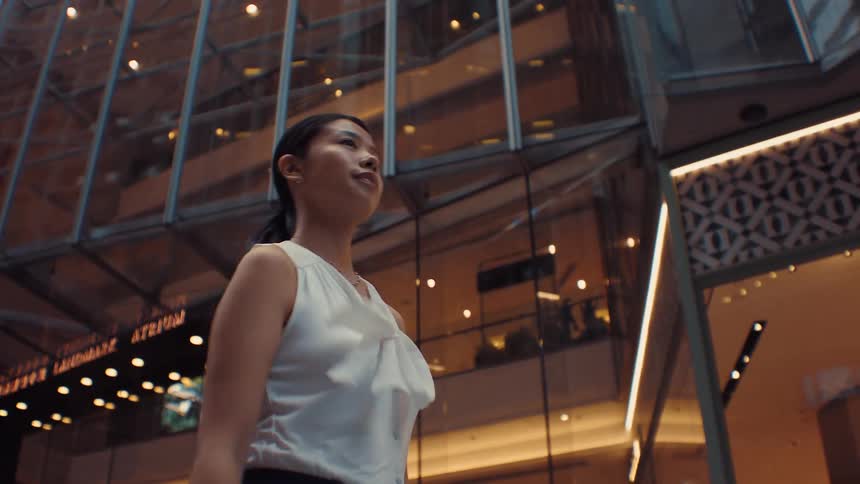 Woman in white blouse walking past illuminated glass facade