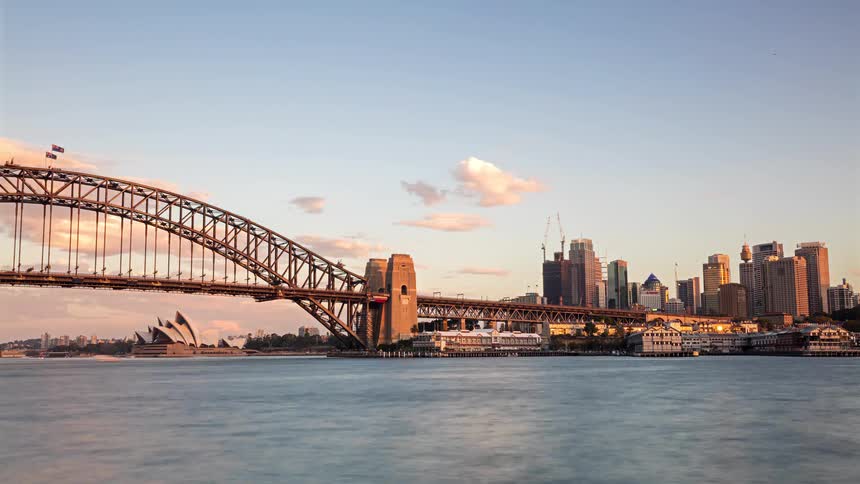 Sydney harbour bridge lit at dusk with urban skyline and sydney opera house by the waterfront