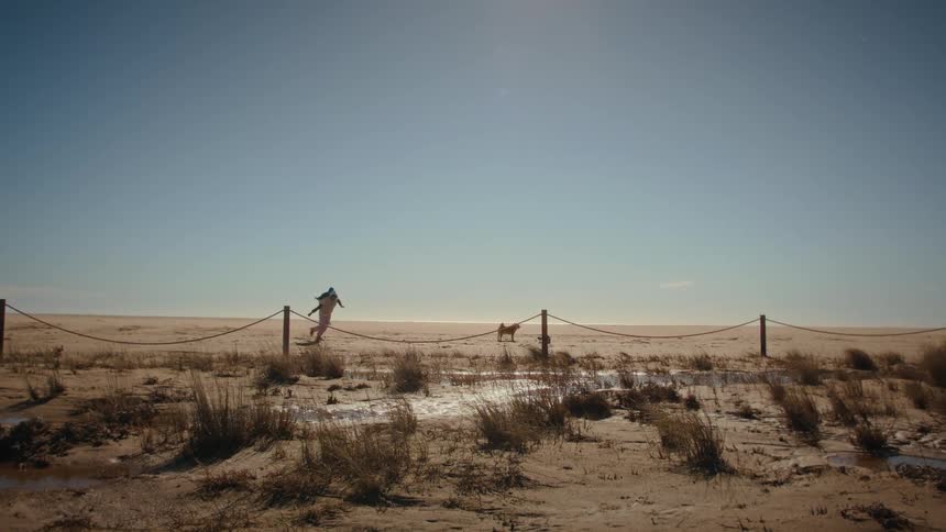 Woman carries her child on her back playing as their dog stands on the beach