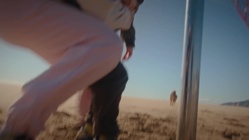 A mother playing with her son on the beach lifting him and gently falling onto her back in the sand with a dog walking nearby on a sunny day